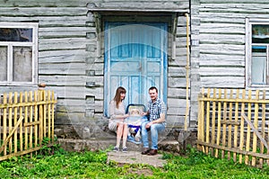 Portrait of young happy family with baby kid in baby carriage sitting together in front of old retro wooden house