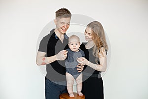 Portrait of young happy family in dark clothes with plump cherubic baby infant toddler standing on white background. photo