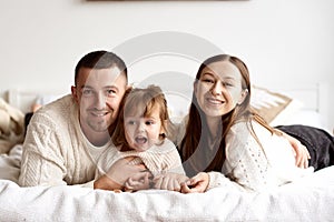 Portrait of a young happy family lying in bed smiling and looking at the camera