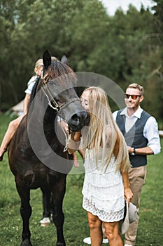 Portrait of a young happy family, parents and children, having fun at countryside outdoors, walking with horse. Kids are