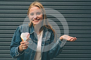 Portrait of young happy girl eating ice-cream, outdoor, over blue wall background.