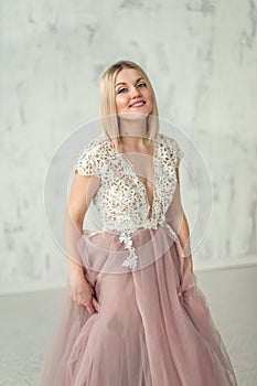 Young happy girl in an evening dress with lace and pink fartine on the background of a white textural wall. Close up