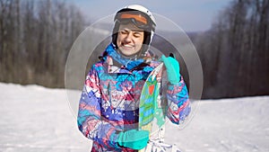 Portrait of a young, happy girl with a snowboard in her hands. Winter sunny day, around the mountain, ski resort. A