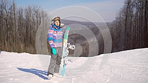 Portrait of a young, happy girl with a snowboard in her hands. Winter sunny day, around the mountain, ski resort. A