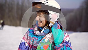 Portrait of a young, happy girl with a snowboard in her hands. Winter sunny day, around the mountain, ski resort. A