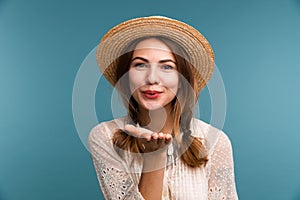 Portrait of a young happy girl in summer hat isolated over blue background, looking at camera