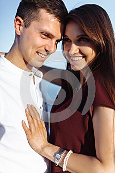 Portrait of a young, happy, loving couple standing on stones at sea, in the arms, and looking at each other, advertising and inser