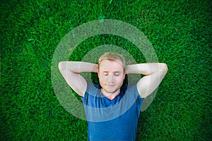 Portrait of a young happy man with closed eyes relaxing on the grass with his hands under the head. Selective focus.