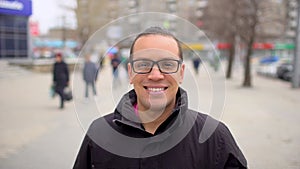 Portrait of young happy man with glasses looking to the camera and smiling on the city background. Close up portrait of