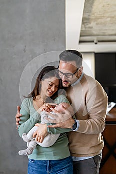 Portrait of young happy man and woman holding newborn cute babe dressed in white unisex clothing.