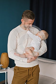Portrait of a young happy man holding his cute baby in his arms. Caucasian father gently hugs his charming little son and smiles.