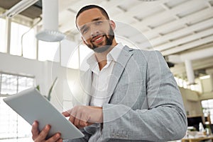 Portrait of a young happy mixed race businessman working on a digital tablet in an office. One hispanic male boss