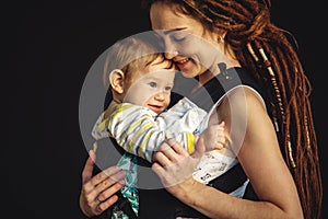 Portrait young happy mom with baby son in ergo backpack on dark wall on the background