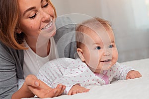 Portrait of a young happy mother lying with her baby on the bed. Close up. Concept of motherhood and child care