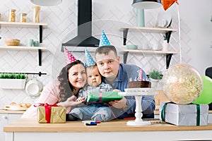 Portrait of young happy parents celebrating their little son`s first birthday at home birthday party