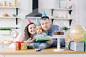 Portrait of young happy parents celebrating their little son`s first birthday at home birthday party