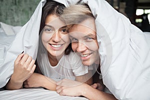 Young couple in bed looking at camera covered with blanket