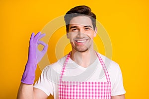 Portrait of young happy positive good mood smiling man in gloves showing okay sign isolated on yellow color background