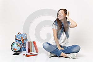 Portrait of young happy pretty woman student with closed eyes correcting hairstyle sitting near globe, backpack, school