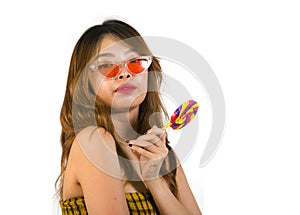 Portrait of young happy and Asian Korean girl in cool fashion sunglasses eating lollipop candy posing naughty teasing