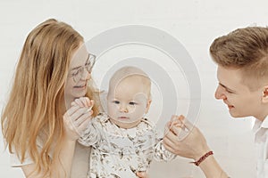 Portrait of young happy smiling beautiful family with cherubic blue-eyed infant baby toddler in white clothes sitting. photo