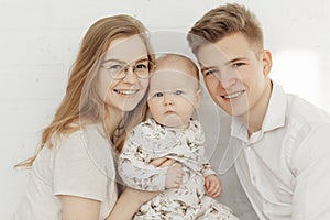 Portrait of young happy smiling beautiful family with cherubic blue-eyed infant baby toddler in white clothes sitting. photo