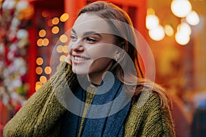 Portrait of young happy smiling woman enjoying by holiday glowing garlands on street