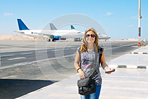 Portrait of young happy smiling woman with a passport at the airport with three plains on background on summer day. Travelling and