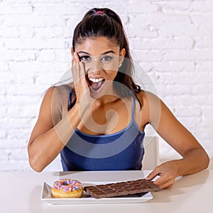 Portrait of young happy woman eating delighted chocolate bar and donuts