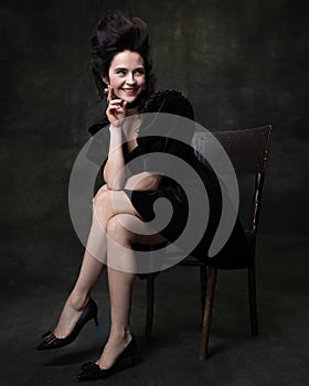 Portrait of young happy woman in image of medieval royal person in black dress isolated on dark vintage background.