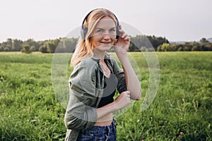 Portrait of young happy woman listening to music with headphones and smiling on a green grass outdoor. Music lover