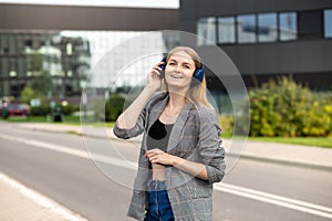 Portrait of young happy woman listening to music with headphones and smiling while walking on the street in the city