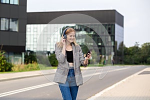 Portrait of young happy woman listening to music with headphones and smiling while walking on the street in the city