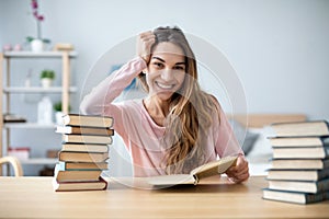 Portrait of young happy woman sits at a table with books studying at home