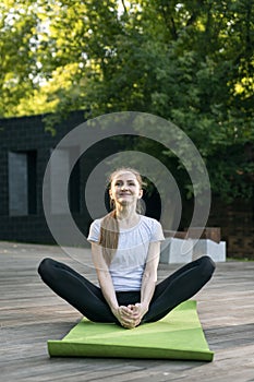 Portrait of young happy woman sitting on yoga mat in butterfly position in green park. Baddha Konasana. Yoga for beginners