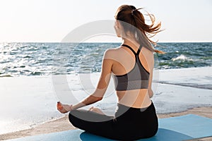 Portrait of young healthy woman sitting in lotos pose while practicing meditation at seaside