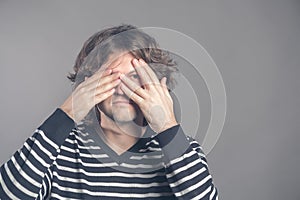 Portrait of young hipster man in sweater peeping at the camera through his fingers. Picture of embarrassed male looking