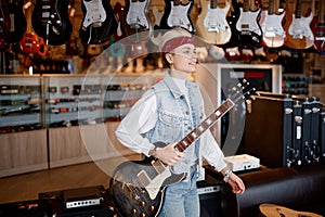 Portrait of young hipster woman musician with guitar at professional shop