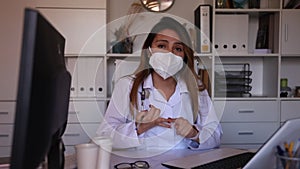 Portrait of young hispanic female doctor in face mask making welcome gesture welcoming patient to clinic