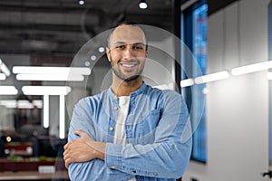 Portrait of a young hispanic male programmer and developer standing in the office, crossing his arms over his chest and