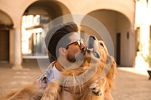 Portrait of young Hispanic man with beard and sunglasses kissing his dog which he is holding in his arms very happy. Concept