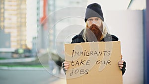 Portrait of young homeless man with cardboard looking at camera and very upset because of immigrants crisis in Europe