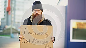 Portrait of young homeless man with cardboard sing standing at the street