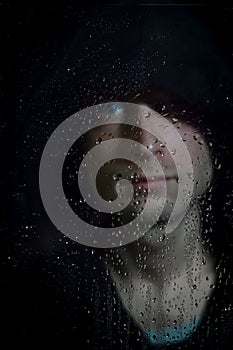 Portrait of a young hooded man behind glass covered in water drops - focus on the droplets