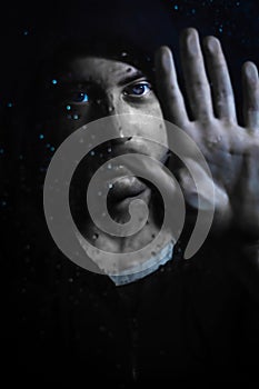 Portrait of a young hooded man holding his hand on a glass covered in water drops - focus on his face