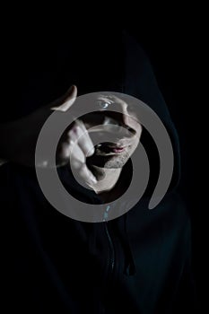 Portrait of a young hooded man making a sign of the horns with his hand in the shade