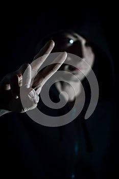 Portrait of a young hooded man making a victory sign with his fingers, focus on the hand