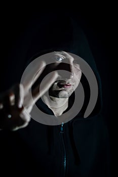 Portrait of a young hooded man making a victory sign with his fingers, focus on his eyes