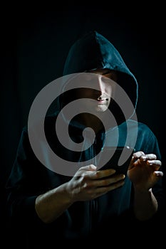 Portrait of a young hooded man who is using a smartphone