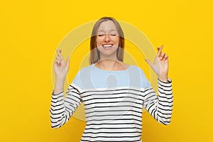 Portrait of young hopeful woman cross fingers, making wish, hoping for smth, wishing, standing over yellow background with